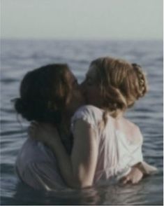 two women in the water kissing each other with their arms around one woman's neck