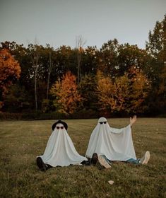 two people dressed up like ghostes sitting in the grass