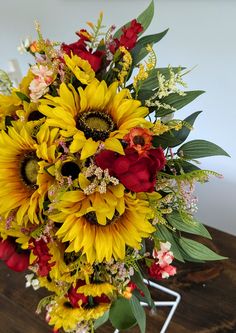 a bouquet of sunflowers and other flowers in a vase on a wooden table