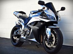 a silver motorcycle parked in front of a white wall with black rims on it