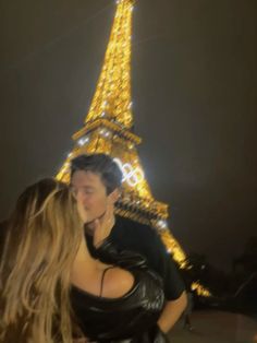 a man and woman standing in front of the eiffel tower at night with their arms around each other