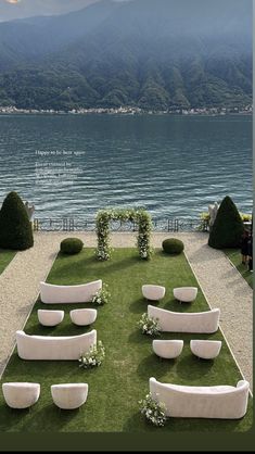 an outdoor wedding setup with white couches and greenery on the lawn by the water