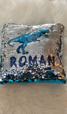 a blue and silver sequinized pillow with a dinosaur on it that says roma