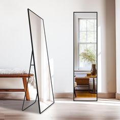 a mirror sitting in the middle of a room next to a table with a vase on it