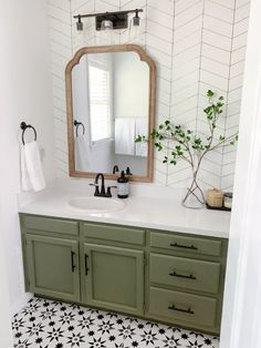 a bathroom with black and white flooring and green cabinetry, along with a large mirror over the sink