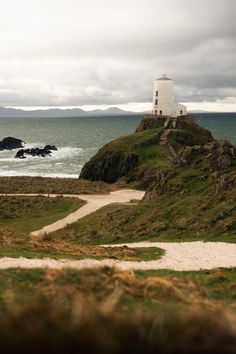 a white lighthouse sitting on top of a green hill next to the ocean