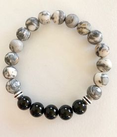 "Natural matte grey Picasso jasper and polished black onyx gemstones on a stretch bracelet. Men's handsome stretch bracelet of 10mm matte grey and white Picasso jasper and 10mm polished black onyx gemstones. Silver pewter wheel spacers add extra accents Bracelet is made to order on professional stretch elastic. When selecting size please add 3/4\" to 1\" to actual wrist measurement for a comfortable fit. Handsome bracelet for everyday wear!" Casual Black Stretch Bracelet With Gemstone Beads, Adjustable Black Agate Stretch Bracelet, Casual Black Agate Beaded Bracelets, Paris Charm Bracelet, Paris Souvenirs, Black Onyx Bracelet, Surfer Necklace, Wood Bead Necklace, Picasso Jasper