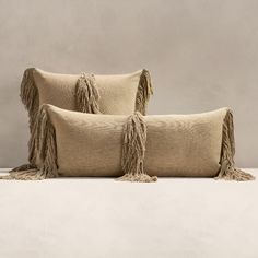 two pillows with fringes on them sitting next to each other