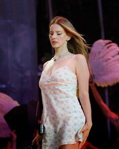 a woman with long hair walking down a runway wearing a white dress and pink flamingos in the background