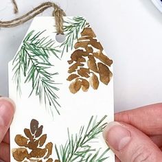 a hand holding a tag with pine cones on it