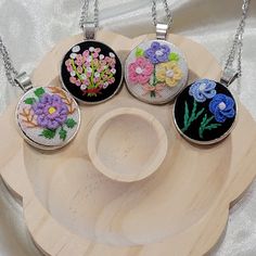 four pendants with flowers on them sitting on a wooden plate