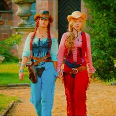 two women dressed in western clothing walking down a dirt road