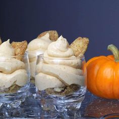 three glasses filled with dessert sitting on top of a table next to an orange pumpkin