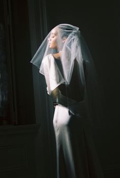 a woman wearing a veil and dress standing in front of a window