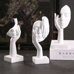 three small white sculptures on top of a black table next to a box with the word barber written on it