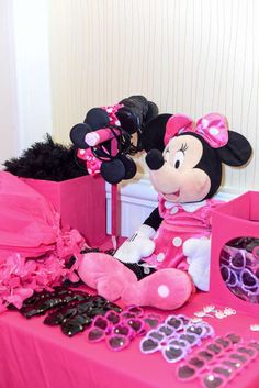 a minnie mouse stuffed animal sitting on top of a table next to pink bags and other items