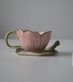 a pink and green tea cup sitting on top of a saucer with two handles