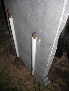 two white poles sticking out of the side of a metal structure with grass and dirt around them