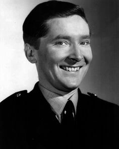 a black and white photo of a man in uniform smiling at the camera with a smile on his face