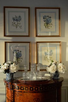 three framed pictures on the wall above a table with vases and flowers