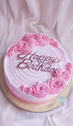 a birthday cake with pink frosting and roses on it sitting on a white cloth