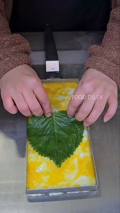 a person cutting up a green leaf on top of a metal tray with yellow liquid