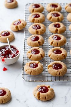 peanut butter and jelly cookies cooling on a wire rack with a bowl of jam in the background