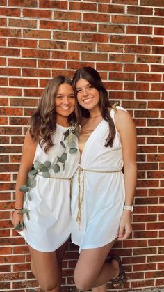 two women standing next to each other in front of a brick wall wearing white dresses