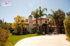 a woman standing in front of a large house with palm trees on either side of her