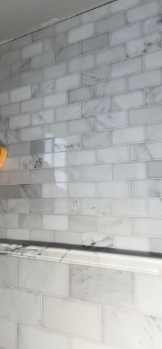 a light that is on in the corner of a room with white tile and marble