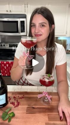 a woman holding a drink in her hand while sitting at a kitchen counter with two glasses