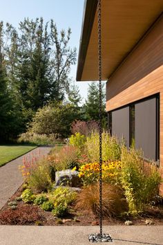 an outdoor garden with flowers and plants on the side of a house, next to a walkway