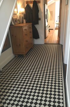 a hallway with black and white checkered flooring next to a wooden dresser in the corner