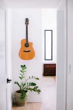 a guitar hanging on the wall next to a potted plant and door way in a house