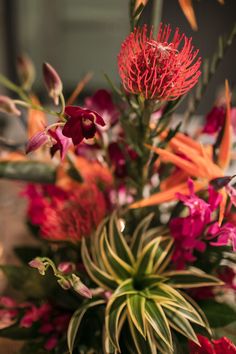 a vase filled with red and pink flowers on top of a wooden table covered in greenery