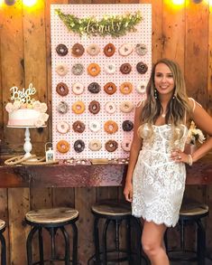 a woman standing in front of a table with donuts on the wall behind her