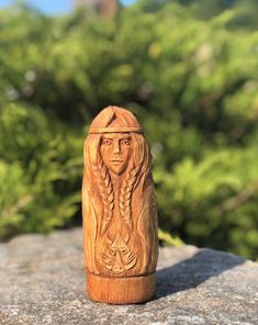 a carved wooden doll sitting on top of a rock next to some bushes and trees