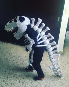 a person in a dinosaur costume standing next to a wall with a skeleton on it