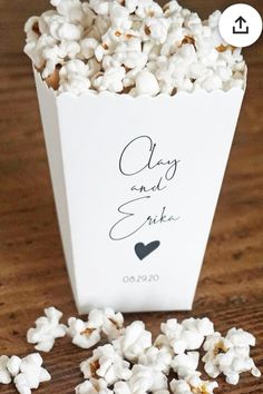 a small white box filled with popcorn sitting on top of a wooden table next to a couple's names