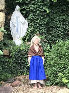 a woman standing in front of a statue and shrubbery with a blue skirt on