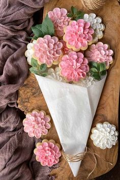 cookies decorated with pink and white flowers are on a wooden platter next to a napkin