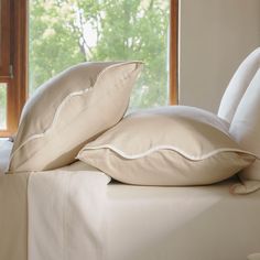 two pillows on top of a bed next to a window with trees in the background