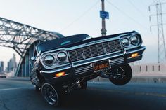 an old black car driving down the road with its hood up and lights turned on