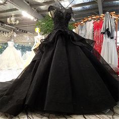 a black ball gown is on display in a clothing store, with other dresses behind it