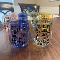 four wine glasses with words on them sitting on a wooden table in front of a window