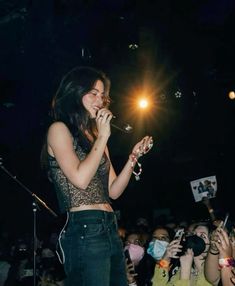 a woman standing in front of a crowd holding a microphone and singing into a mic