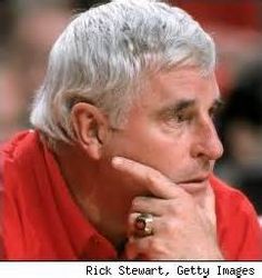 an older man with grey hair wearing a red shirt looking off to the side while holding his hand on his chin