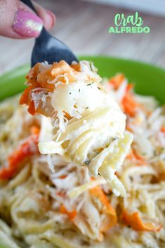 a spoon full of pasta with carrots and parmesan cheese on top is being lifted from a green bowl