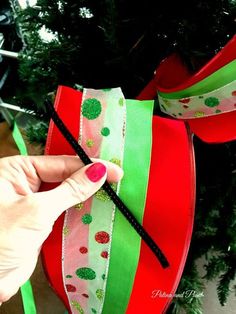 a hand is holding a green and red ribbon near a christmas tree with decorations on it