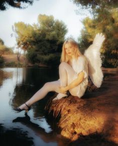 a woman sitting on top of a rock next to a body of water with an angel wings